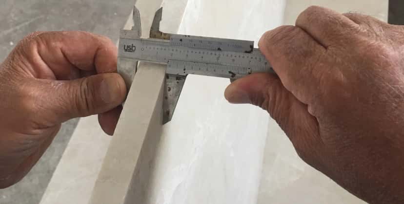 Control de calidad de precisión midiendo grosor de mármol blanco con calibradores profesionales
